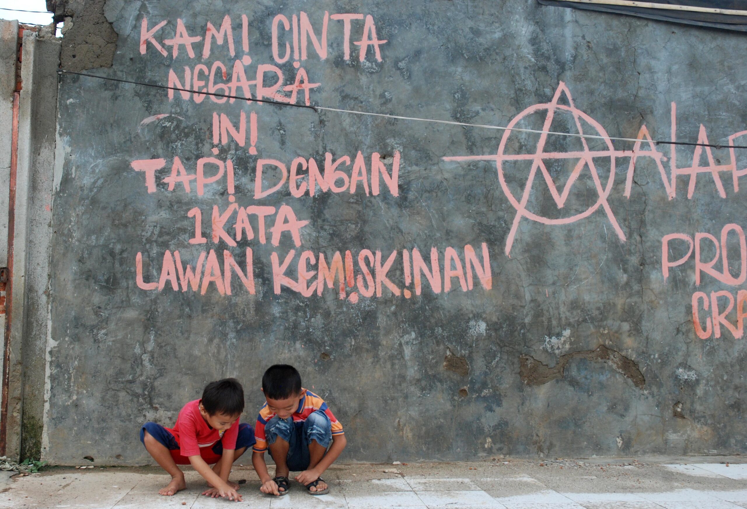 Dua orang bocah, Jumat (06/4) asik bermain dekat dinding bertuliskan " KAMI CINTA NEGARA INI TAPI DENGAN 1 KATA LAWAN KEMISKINAN" di Desa Karet, Kecamatan Sepatan, Kabupaten Tangerang ( M JAKWAN/TANGERANG EKSPRES)