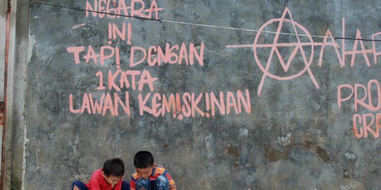 Sebuah tulisan ditembok rumah warga di Desa Karet, Kecamatan Sepatan, Kabupaten Tangerang " KAMI CINTA NEGARA INI TAPI DENGAN 1 KATA LAWAN KEMISKINAN" sementara dua bocah asik bermain disana ( Ragawilapa)